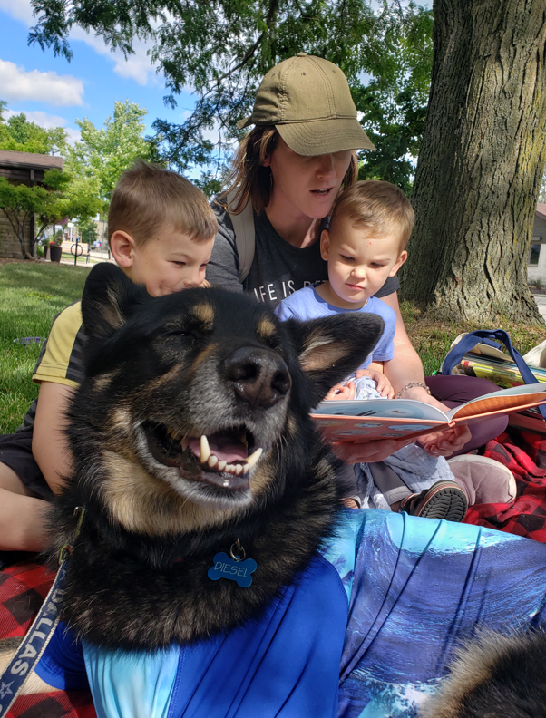therapy dog Diesel with a family reading to him on the library lawn